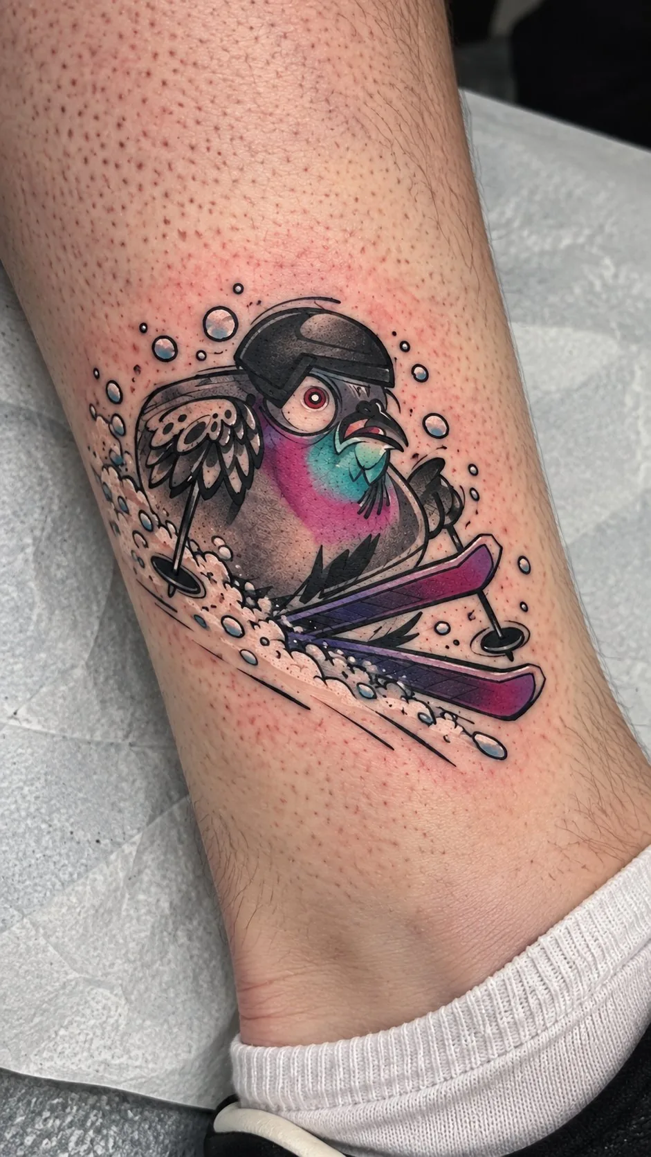 Illustrative skiing pigeon tattoo on the ankle